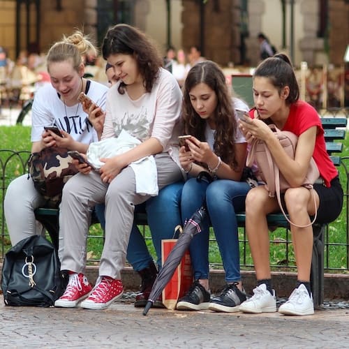 Teenage Anxiety Hypnotherapy for Teenage Anxiety - Four teenagers on a bench using their mobile phones without anxiety